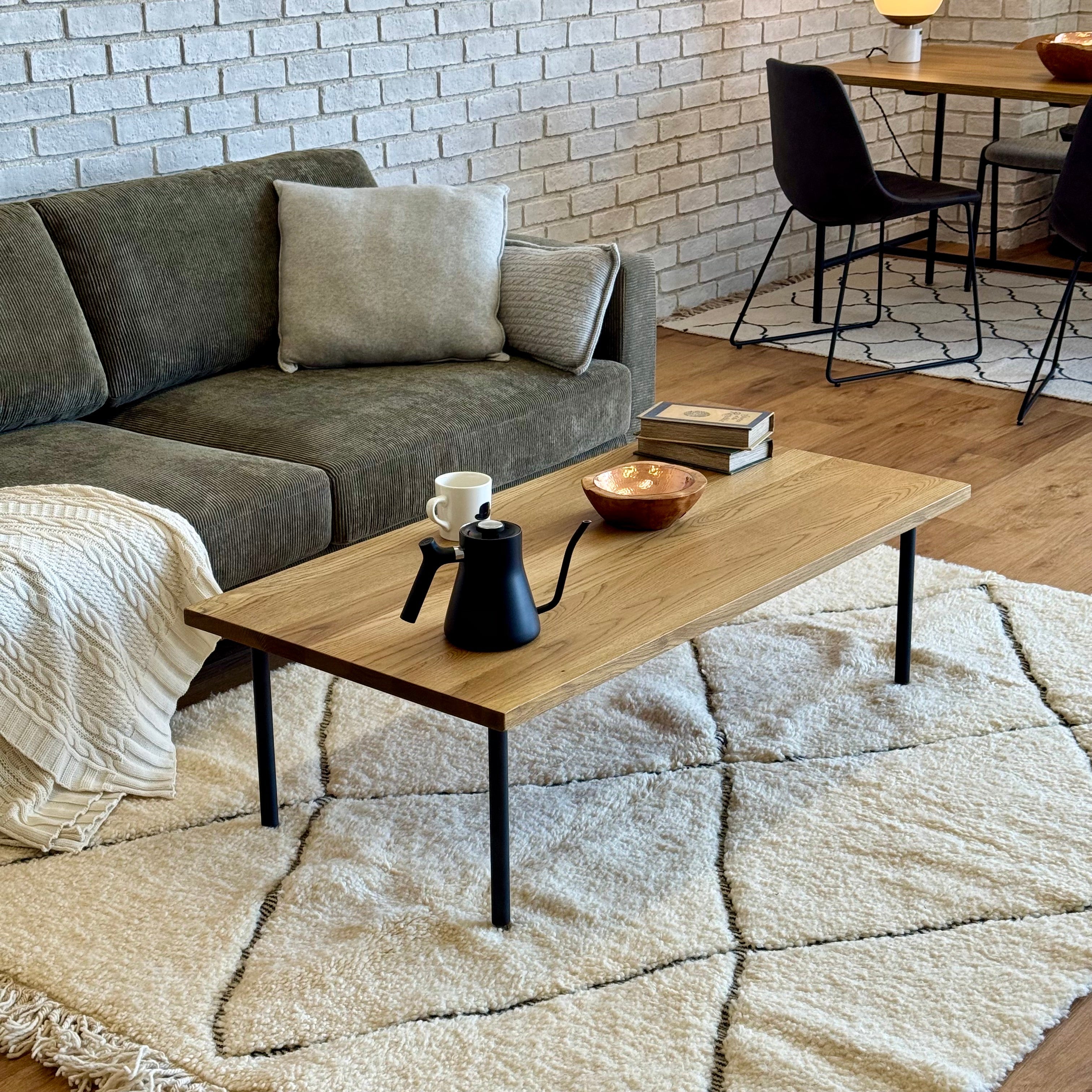BYRON COFFEE TABLE 1200 MBR（W120×D60×H36）をリビングのソファ前に配置した全体写真。ホワイトオーク無垢天板と細身スチール脚の抜け感が分かる。
